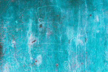 A close-up of a weathered turquoise metal surface with scratches, rust spots, and faded markings....