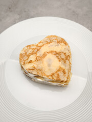 Delicious heart shaped crepes, pancakes  with white yogurt are sitting on a white plate, creating a romantic and tasty breakfast for Mother's Day Valentines copy space
