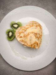 Heart shaped crepes, pancakes served with sliced kiwi fruit and honey on white plate, delicious breakfast or brunch for Mother's Day Valentines copy space