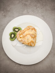 Heart shaped crepes with white yogurt, pancakes drizzling honey, garnished with kiwi slices, presenting romantic breakfast on pristine white ceramic plate for Mother's Day Valentines copy space