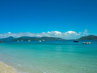 Turquoise waters of the Great Barrier Reef near Green Island with anchored sailboats and yachts against mountainous backdrop. Crystal-clear tropical waters meet coral beach shoreline, Queensland sky