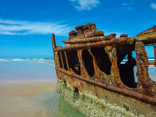 Rusted hull remnants of SS Maheno shipwreck with circular portholes. Turquoise waters. Blue sky on...