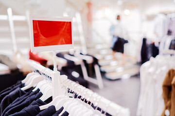 Clothing Store Interior Display With Hanging Garments and Blank Red Sign..