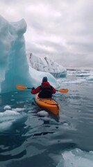 A skilled kayaker navigates icy, clear waters, surrounded by stunning icebergs on a beautiful, sunny day