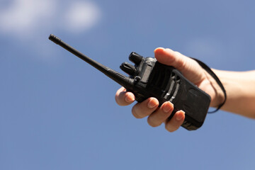 A portable walkie-talkie against a blue sky during a mountain adventure, held in a hand. Dynamic...