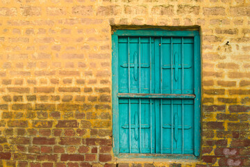 old door yellow wall and blue color door, The image features a vibrant yellow wall with a blue-framed door and two blue-framed windows with white sills. The door has three hinges and a latch, while