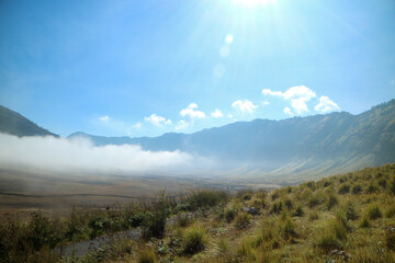 mountain landscape with green grass, morning mist and blue sky