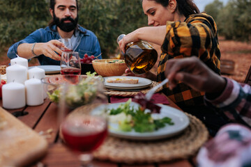 Friends enjoying outdoor meal with wine and olive oil in olive grove