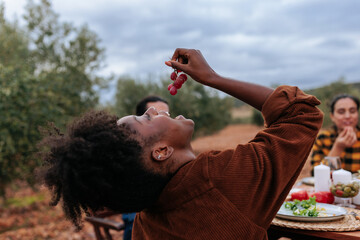 Woman eating grapes at outdoor table with friends in olive grove