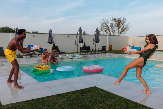 Friends playing with water guns by the pool during summer holidays