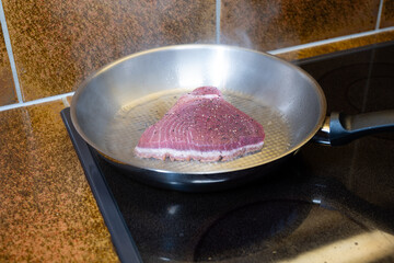 Fresh raw seasoned tuna steak slice being cooked in an aluminum frying pan. Close up shot, no people