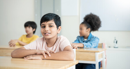 Portrait of little asian Indian boy pupil smile at desk in classroom at elementary school. Student boy study in international primary school. Children learn lesson in classroom. Education knowledge