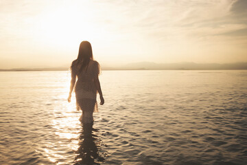 Fototapeta premium woman advances in the lake wrapped in the golden light and the reflections of the waves