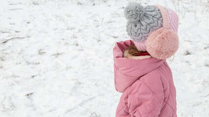 Cheerful positive child girl wearing a outerwear smiling walking through a snowy countryside forest
