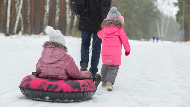 Father and daughters ride downhill on a Snow tubing in the park on the winter holidays