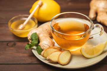 Cup of hot ginger tea with slices of ginger root on wooden background. Warming drink. Alternative medicine. Tea with honey, lemon, ginger and mint. Space for text. Copy space