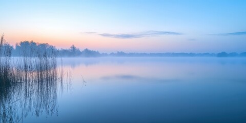Fototapeta premium Serene morning landscape with mist over a calm lake and soft pastel colors in the sky.