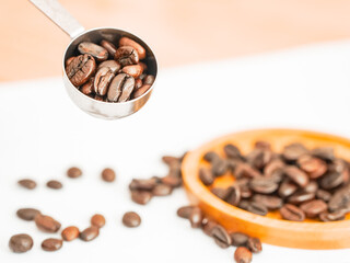Coffee shop business. Dark brown coffee beans on a white background with a coffee scoop and a container. Caffeine-containing plant, bitter taste, brown color, drink ingredients. Popular morning work