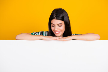 Smiling young woman resting her hands on a white blank surface with vibrant yellow background