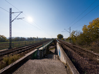 A pair of railway tracks extending into the distance under a bright blue sky, surrounded by autumn...