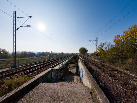 A pair of railway tracks extending into the distance under a bright blue sky, surrounded by autumn foliage and open fields, evoking a sense of travel and adventure.