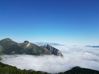 Breathtaking panoramic view of majestic mountains emerging from a sea of clouds under a clear blue sky
