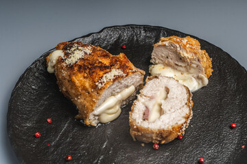 Pieces of chicken cutlet Cordon Bleu with bacon and cheese according to a traditional French recipe on a black mica plate. Space for text.