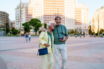 Happy senior couple walking in plaza de espana, madrid, enjoying vacation