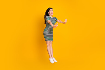 Young woman in striped dress jumping enthusiastically with hands outstretched against a vibrant yellow background