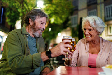 Happy senior couple toasting with beer glasses at outdoor pub