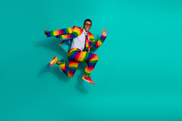 Energetic man in a vibrant rainbow suit jumping in front of a teal background, expressing positivity