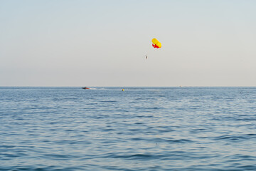 Parasailing in the open sea: a bright parachute pulls a boat, a person enjoys flying over the waves on a sunny day.