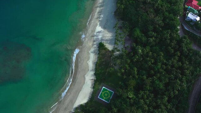 Aerial top down shot of Aninuan Beach with helipad along coastline. Palm trees with villas along Puerto Galera, Philippines.