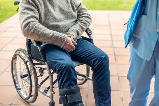 Nurse assisting elderly man in wheelchair with broken leg