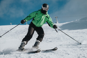 A person in a vibrant green jacket enjoys skiing on a snowy mountain slope under a clear, sunny sky, creating a dynamic and energetic winter sports scene.