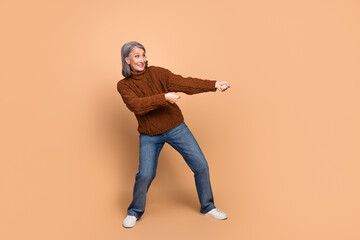 Joyful elderly woman in casual attire making expressive gestures against a beige background