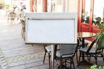 Blank menu board outside a cozy cafe in a vibrant city alley filled with outdoor seating