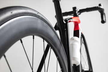 Close-up of a high-performance road bike focusing on the rear wheel, frame, and water bottle against a neutral background.