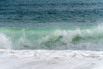 Big sea or ocean wave breaks near the coastline. Windy weather for water sports (surfing, kiting, windsurfing) or calming walks by the beach.