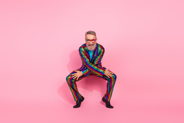 Eccentric senior man in vibrant rainbow suit against pink background, showcasing charisma
