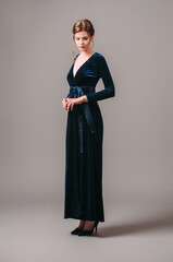 Wrap maxi velour evening dress in navy blue. Long sleeve velvet gown with bow knot. Studio portrait...
