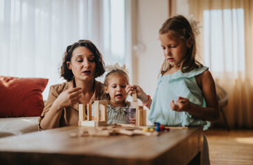 A loving mother spends quality time playing with her two young daughters using wooden blocks. The scene captures a warm and joyful family bonding moment in a cozy home environment.