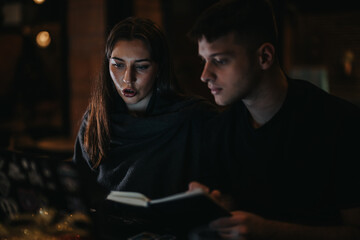 Two individuals reviewing a book together in a dimly lit environment