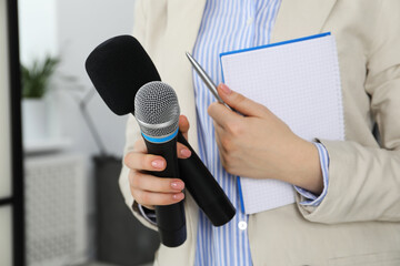 Journalist with microphones, notebook and pen indoors, closeup