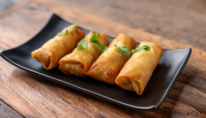 close up fried crispy wrapped spring rolls professionally served on black rectangular plate on wooden table in kitchen tradition asian cuisine