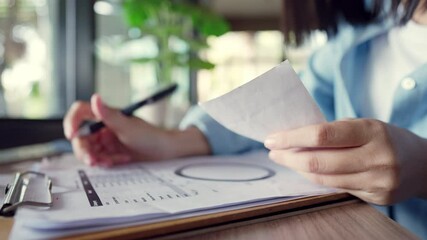 A person is holding a piece of paper and writing on it. Concept of focus and concentration as the person works on the paper. The presence of a potted plant in the background adds a touch of nature