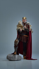 Choice. Full-length portrait of medieval king with crown and sword, standing with determination and pointing forwards against grey studio background. Concept of history, royalty, power, fantasy