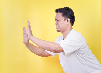 An asian man gestures to stop or push with his hand on a bright yellow background.