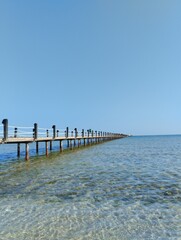 Obraz premium long pontoon bridge extending into the sea, open sea, sea coast, deserted beach without people, bridge on piles