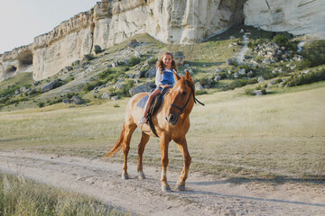 A girl rides a horse near a white rock